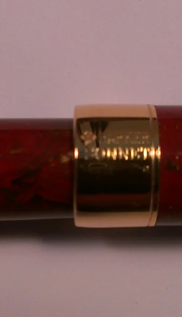 Close-up of the cap band on a red marbled writing instrument showing engraved markings